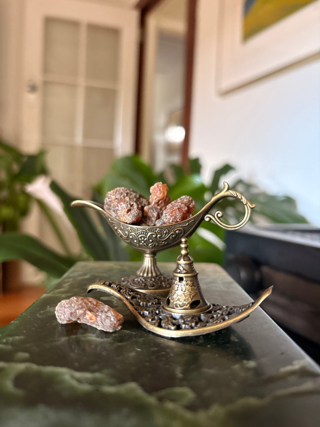 Stone incense holder displaying resin pieces in an ornate brass dish on a green marble surface.