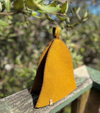 Sauna Hat NZ Wool in vibrant yellow color, displayed on a wooden railing with greenery in the background.